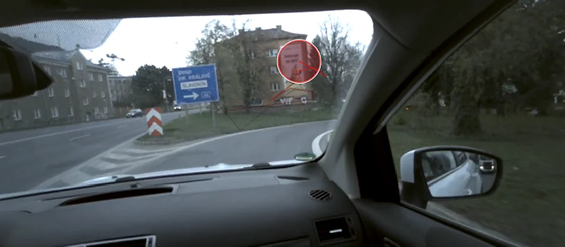 Pohled z auta přes eye-trackingové brýle. Červený kruh ukazuje, kam se respondent právě dívá: na reklamu na budově u silnice.